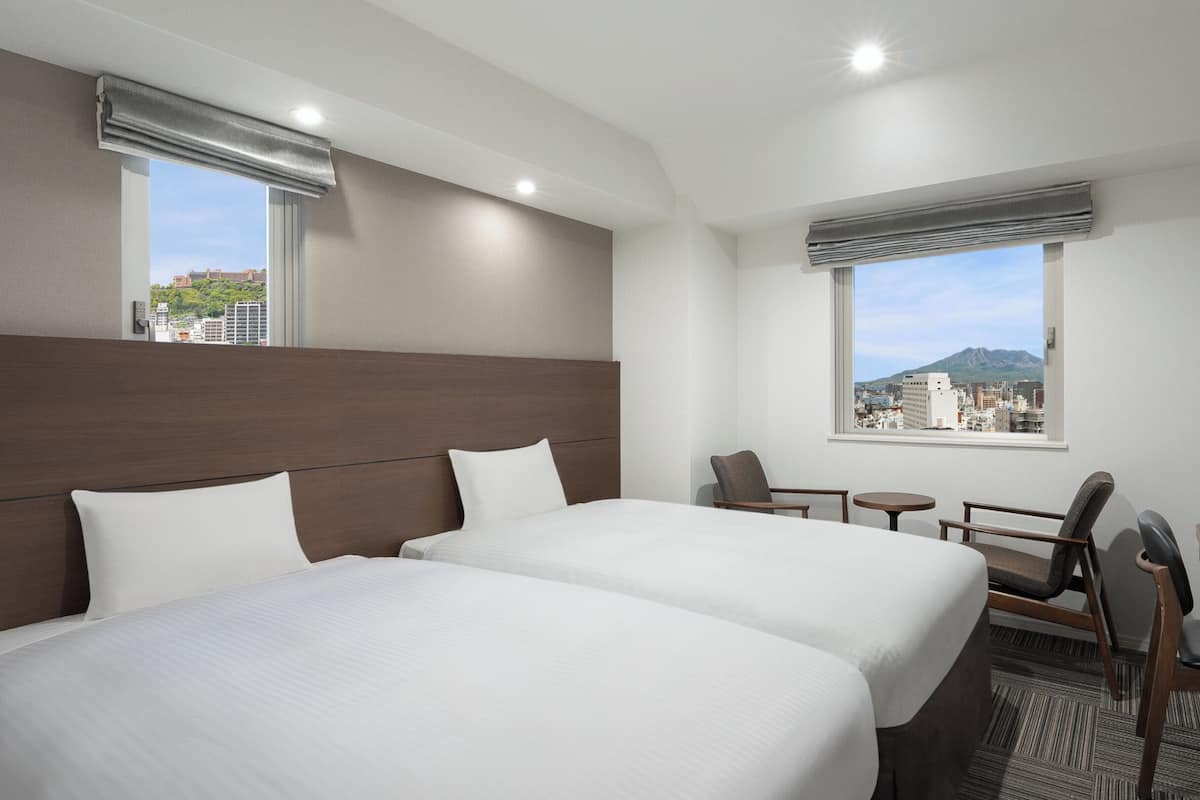 A hotel room with two beds, a desk, a chair, and a TV.