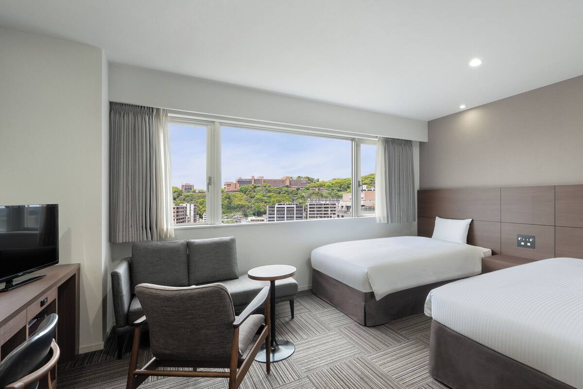 A hotel room with two beds, a TV, a desk, and a chair.