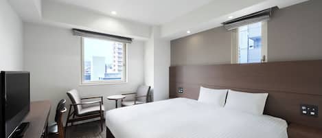 Habitación de hotel con una cama grande, televisión, escritorio, dos sillas y ventana con vista a la ciudad.