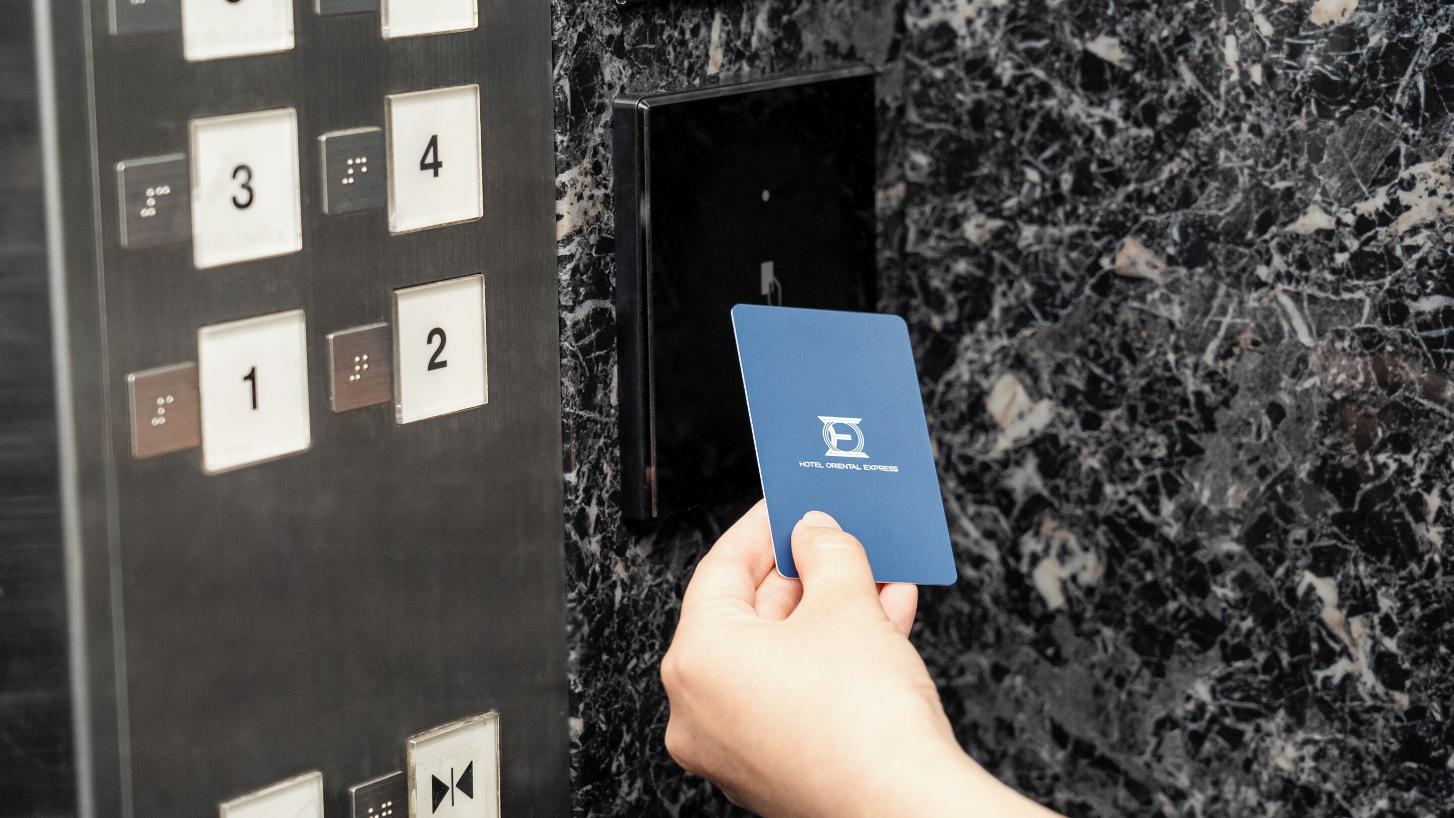 A hand holding a blue card with a logo, inserting it into a slot on a wall with numbered buttons.