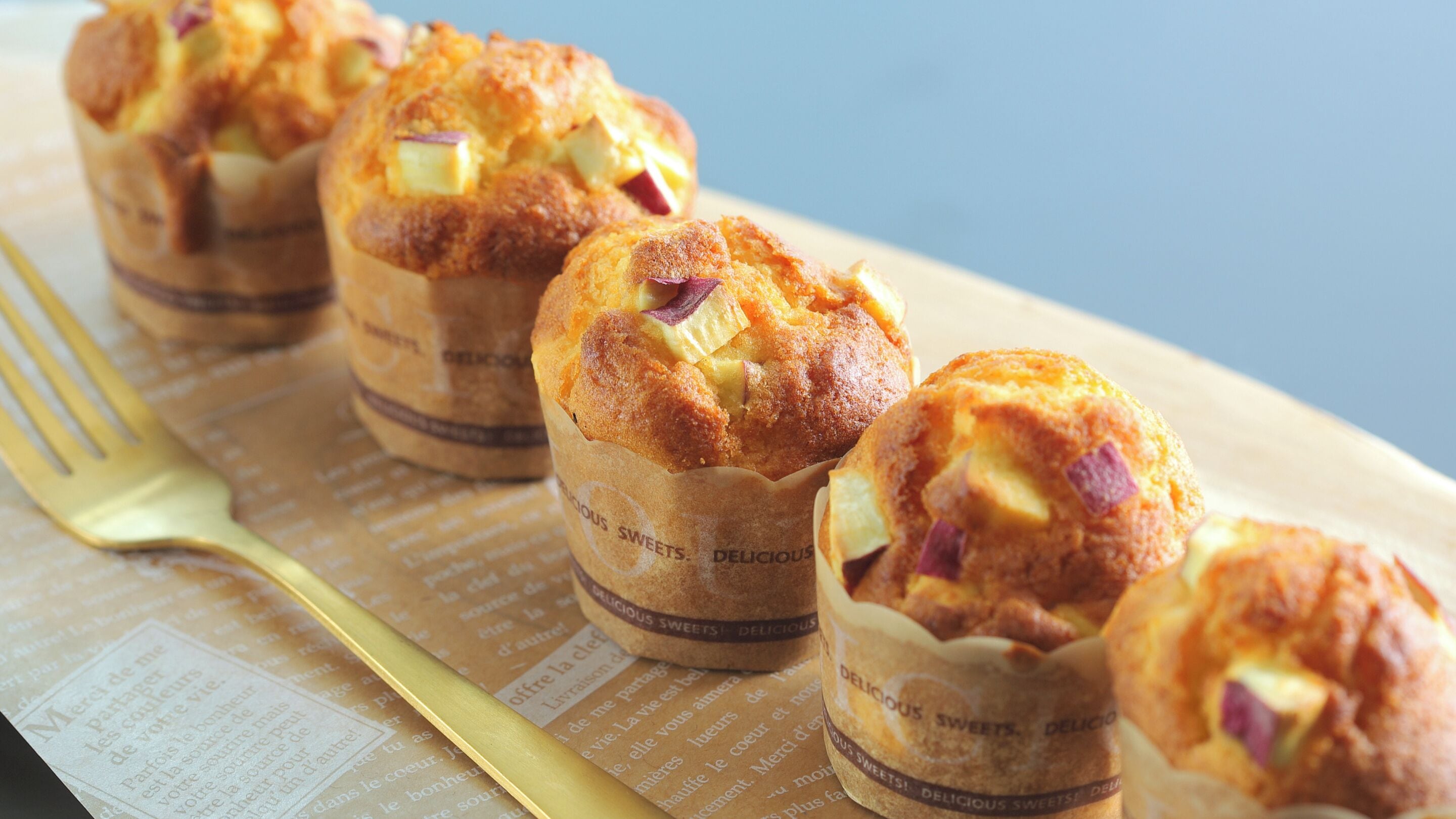 Four muffins in paper cups with a label that reads "DELICIOUS Sweets."
