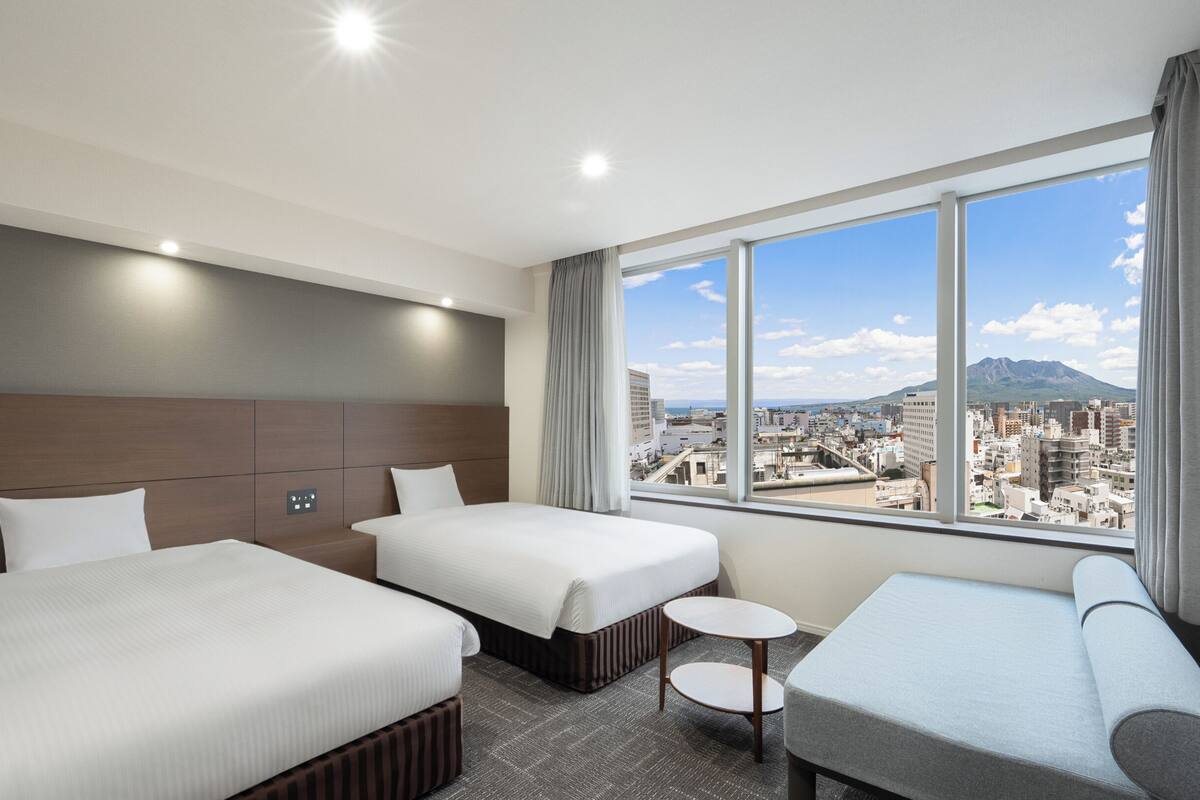 A hotel room with two beds, a TV, a small table, and a sofa.