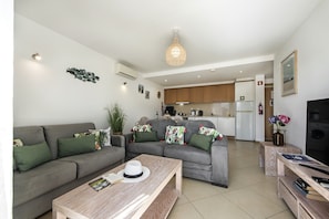 A modern living room with a grey sofa, a wooden coffee table, and a kitchen in the background. - Paradise: Private Balcony with Pool View (Cabanas de tavira)
