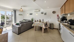 A modern kitchen with a dining area, a grey sofa, and a view of the outside.