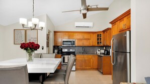Una cocina moderna con armarios de madera, un refrigerador de acero inoxidable y un comedor con mesa y sillas blancas.