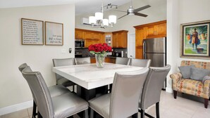 Una cocina moderna con comedor, que incluye una mesa de mármol, sillas tapizadas en gris y un ventilador de techo.