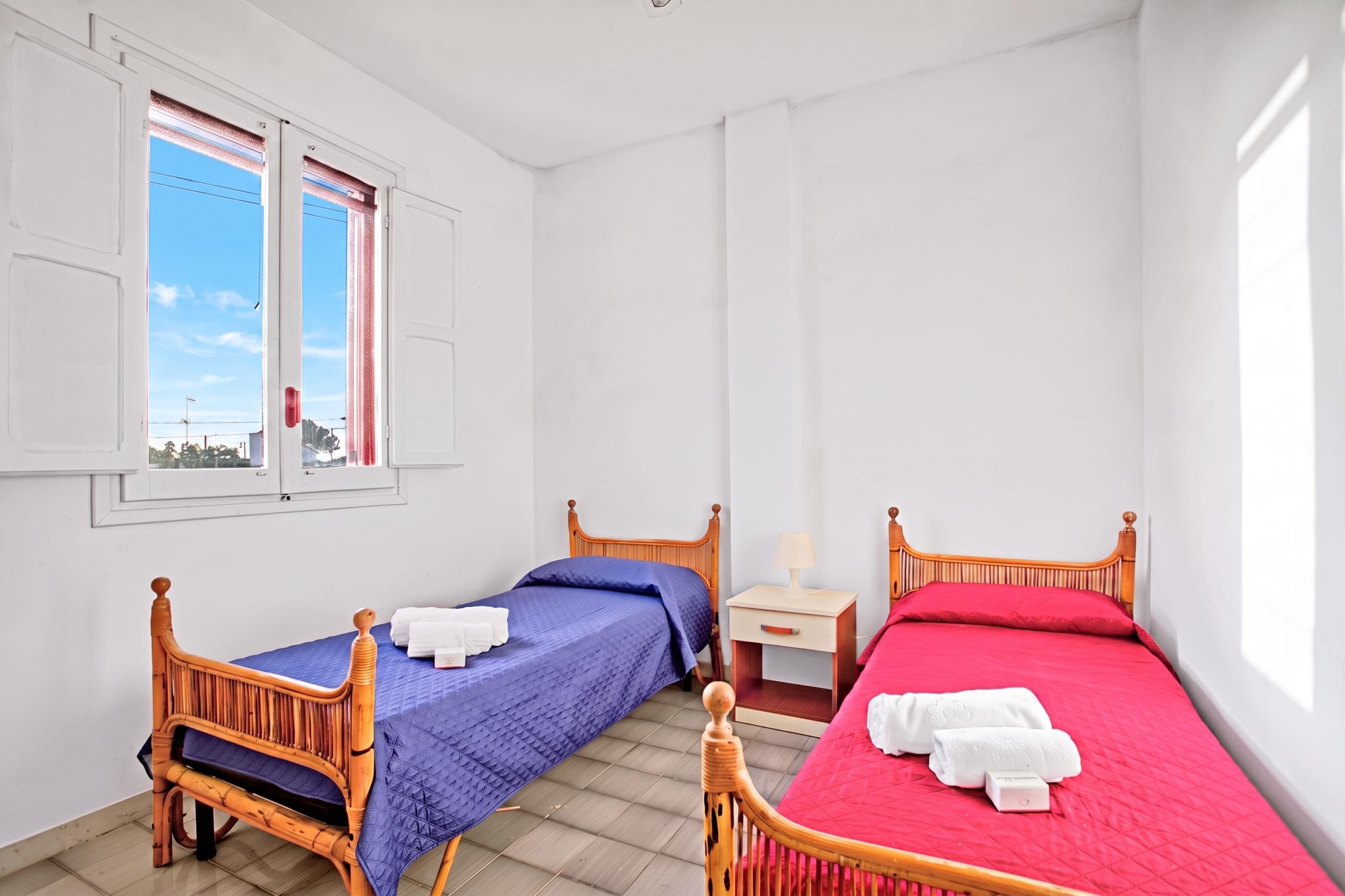 Una habitación con dos camas individuales, una mesita de noche con lámpara y una ventana con persianas.