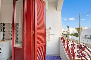 Un balcón con una puerta roja, una lavadora y azulejos con diseño.