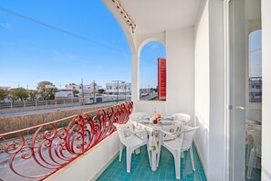 Ein Balkon mit Esstisch, rotem Geländer und Blick auf die Straße sowie auf umliegende Gebäude.
