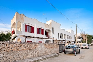 Un edificio blanco con contraventanas rojas y un muro de piedra en primer plano.