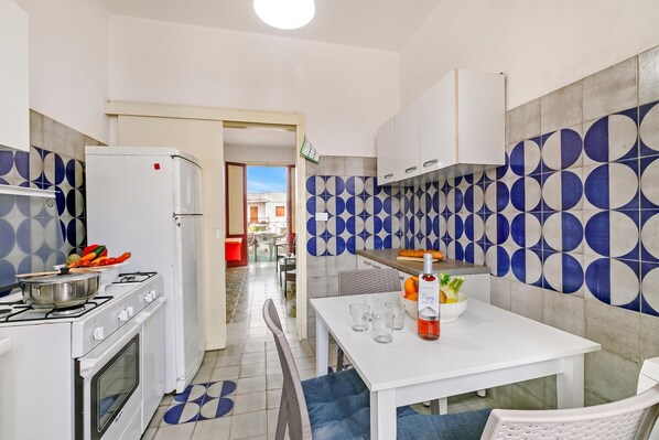 Cocina compacta con estufa a gas, refrigerador y comedor con mesa para dos.