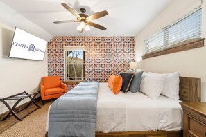 Un dormitorio con cama, una silla, ventilador de techo y ventana.