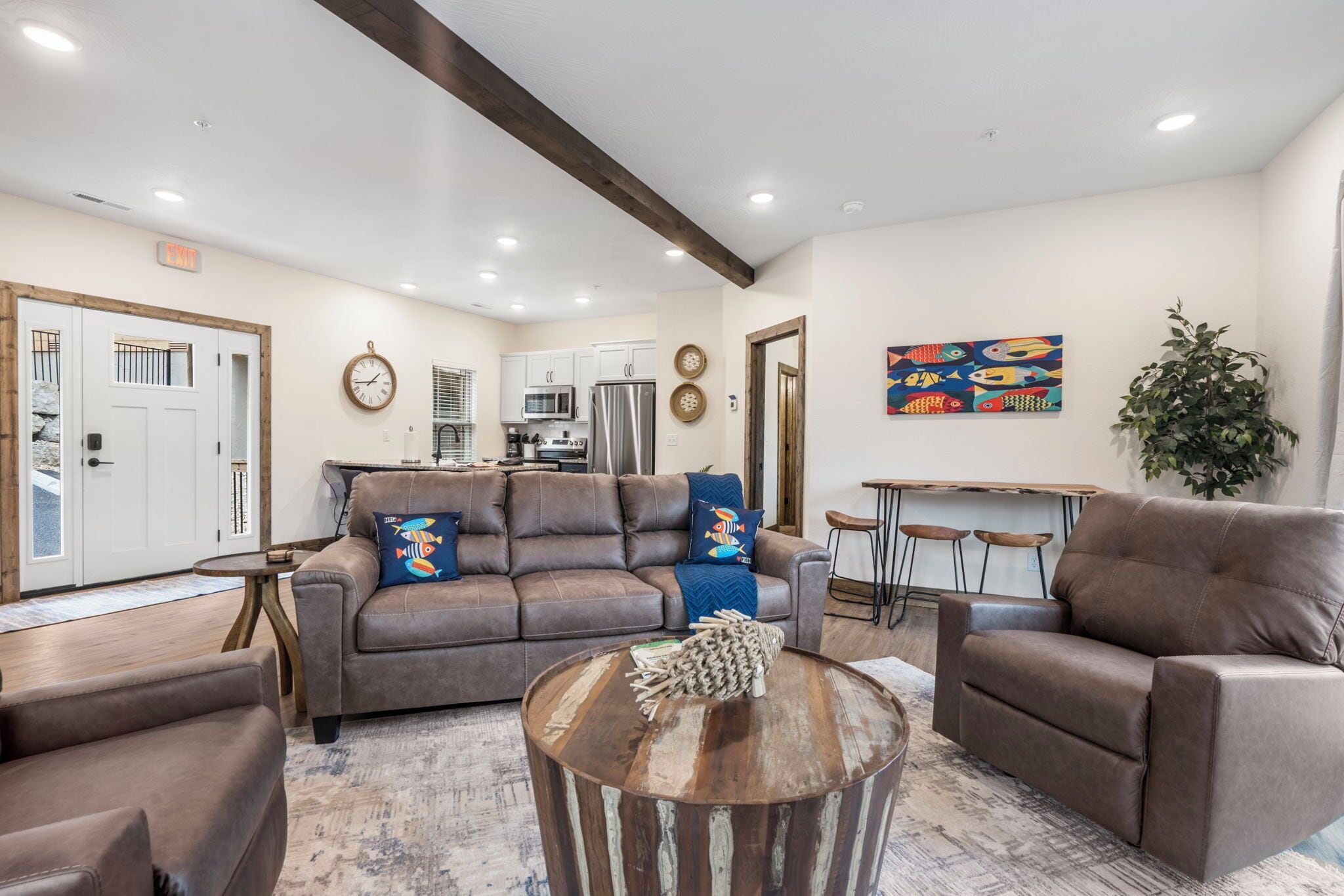 A modern living room with a brown leather sofa, a wooden coffee table, and a dining area with a bar stool.