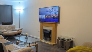 Ett modernt vardagsrum med en platt-TV monterad ovanför en öppen spis, lädersoffor, ett soffbord i glas och en minimalistisk inredningsstil.