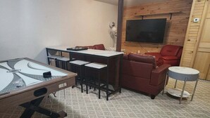 A room with a pool table, a sofa, a red armchair, a small round table, and a mounted television. - Private Home in the White Mountains! (Campton)