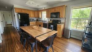 A kitchen with wooden cabinets, a dining table with chairs, a refrigerator, a microwave, and a stove. - Private Home in the White Mountains! (Campton)