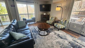 A living room with a leather sofa, a round coffee table, striped armchairs, a TV, and a fireplace. - Private Home in the White Mountains! (Campton)