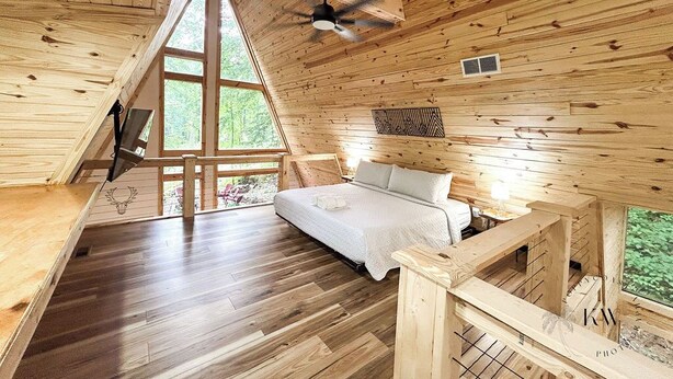 A wooden cabin with a loft bedroom, a ceiling fan, and a large window. - Modern A-Frame-Hot Tub-Gaming Area-EV Charger-10 Minutes to Slade (Stanton)