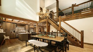 Ein geräumiger Essbereich mit einem Holztisch und Bänken, eine Treppe mit Holzgeländern und eine Küche im Hintergrund.