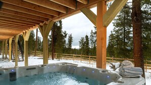 Ein Whirlpool unter einer Holzpergola mit verschneiter Landschaft und Bäumen im Hintergrund.