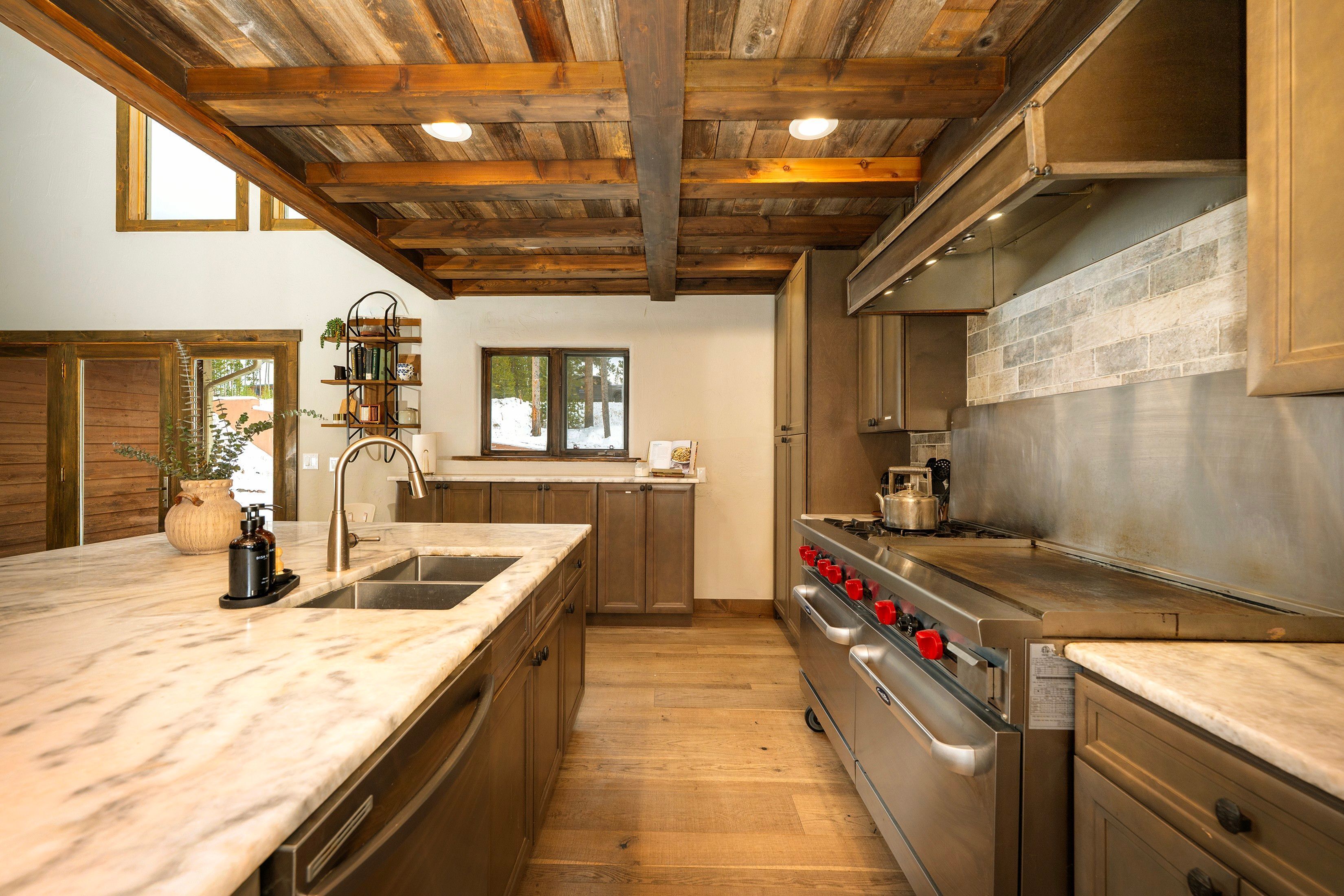 A kitchen with wooden beams, a marble countertop, stainless steel appliances, and a view of the outdoors.