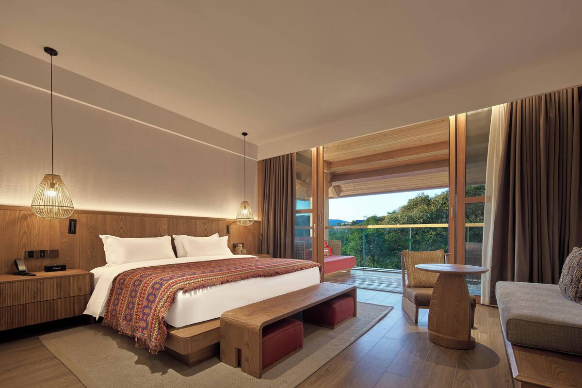 A modern bedroom with a large bed, wooden headboard, and a view of the outdoors.