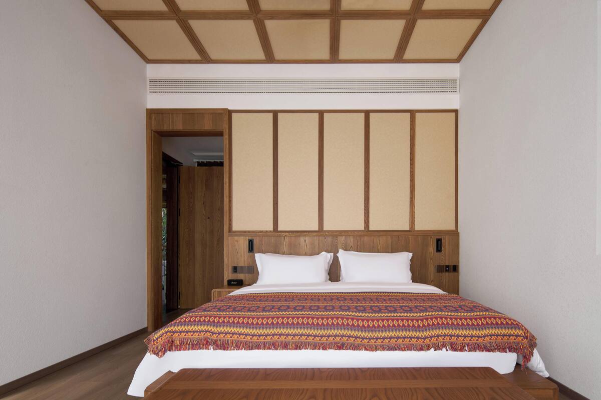 A bedroom with a wooden headboard, a patterned bedspread, and a wooden floor.