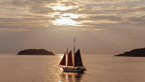 En segelbåt på stilla vatten med en solnedgång i bakgrunden.