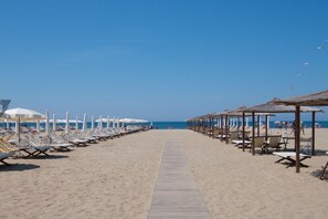 Ein Strand mit Reihen von Liegestühlen und Sonnenschirmen, einem Holzsteg und Strandkörben.