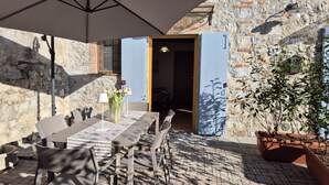 Et udendørs spiseområde med et bord, stole, en stor parasol og en potteplante.