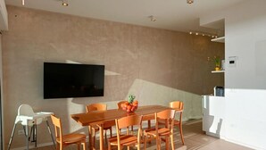 A modern dining area with a wooden table and chairs, a flat-screen TV mounted on the wall, and a small kitchen area with a white refrigerator. -  Elegant and modern seafront flat in Lido di Camaiore, located on the 4th floor with lift, perfect for a relaxing and comfortable holiday.The flat boasts a large terrace with sea view, equipped with an awning and dining table, ideal for enjoying panorami (Camaiore)