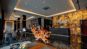 A hotel lobby with a reception desk, seating area, and a decorative wooden sculpture. - The Quadrant Hotel KNO (Medan)