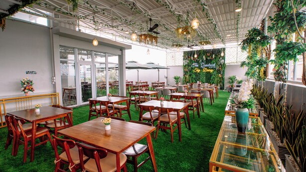 A restaurant with wooden tables and chairs, green artificial grass, and hanging plants. - The Quadrant Hotel KNO (Medan)