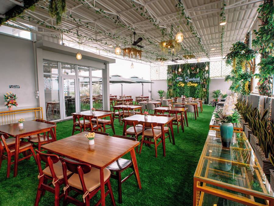 A restaurant with wooden tables and chairs, green artificial grass, and hanging plants.