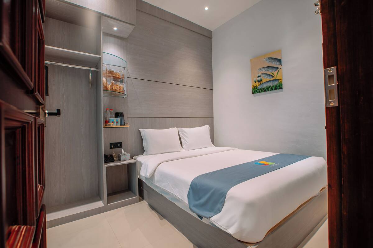 A modern hotel room with a large bed, a bedside table, a nightstand, and a built-in wardrobe.