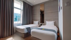 A hotel room with two beds, a large window with curtains, a wooden headboard, and a nightstand with a lamp. - The Quadrant Hotel KNO (Medan)