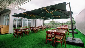 An outdoor patio with green artificial grass, wooden tables and chairs, and large green umbrellas. - The Quadrant Hotel KNO (Medan)