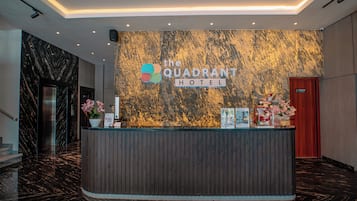 A reception desk at The Quadrant Hotel with a marble wall backdrop, a wooden reception desk, and a red door.