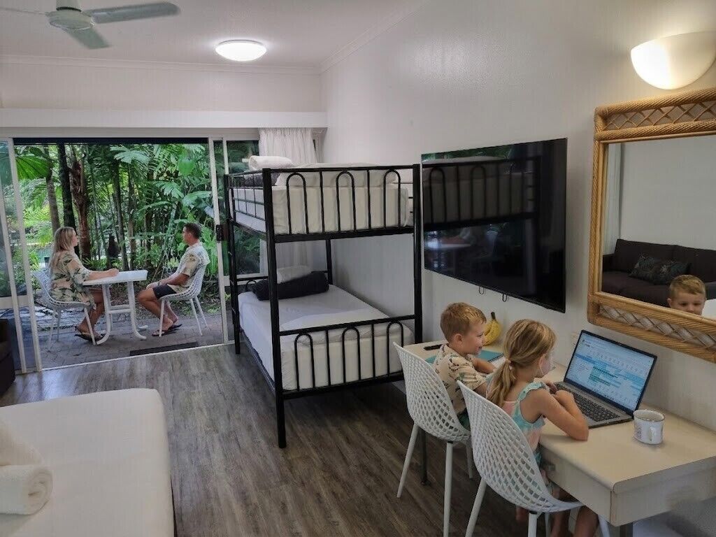A room with bunk beds, a desk with a laptop, and a window overlooking greenery.