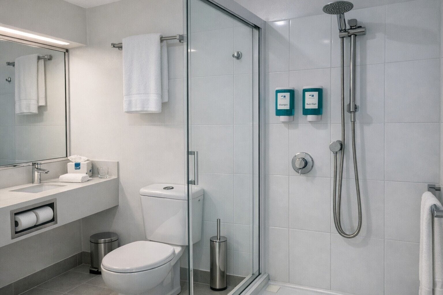 Une salle de bain moderne avec une douche à parois de verre, des toilettes, un lavabo avec un miroir et deux distributeurs de produits de toilette.