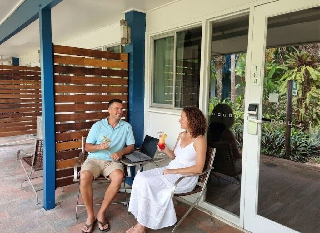 Dos personas sentadas en un banco frente a un edificio con cerca de madera y puerta de cristal.