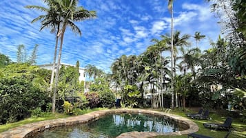Relax by the serene pool surrounded by lush tropical vegetation and lounge chairs.