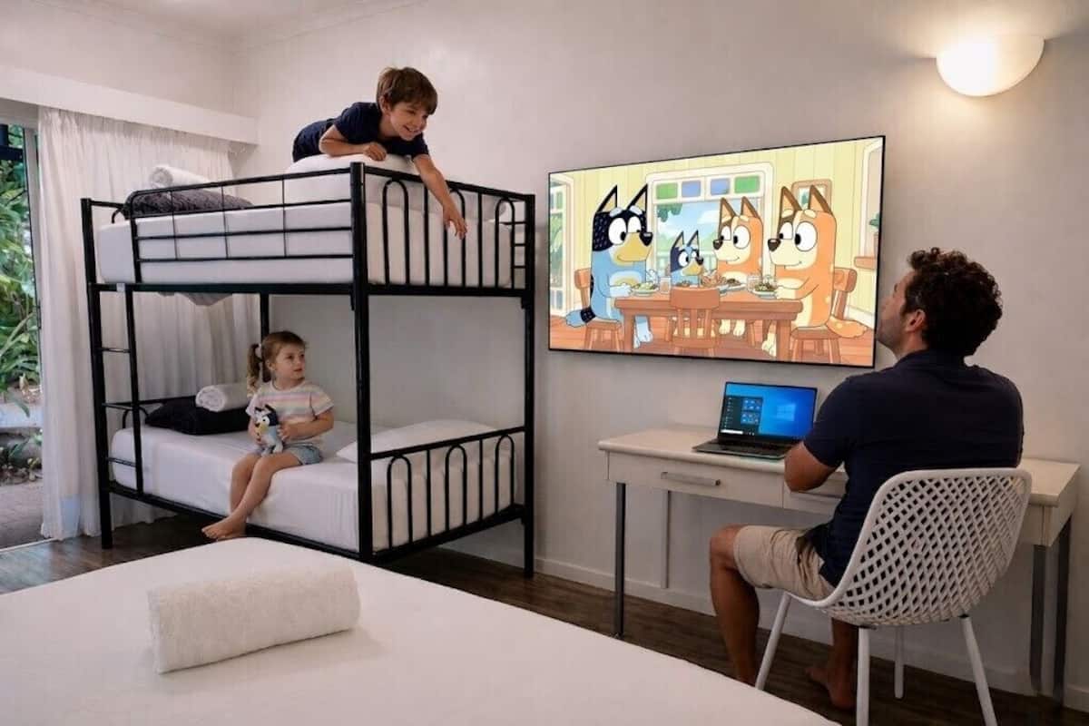 A bunk bed room with a laptop on a desk, a TV on the wall, and a window with curtains.