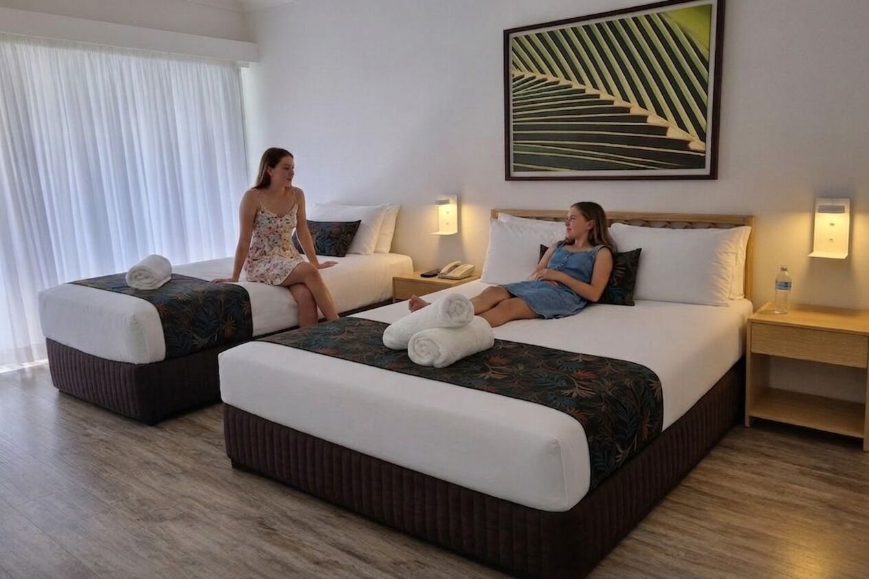 A hotel room with two beds, each with a pillow and a rolled towel. There is a painting on the wall and a nightstand with a lamp.
