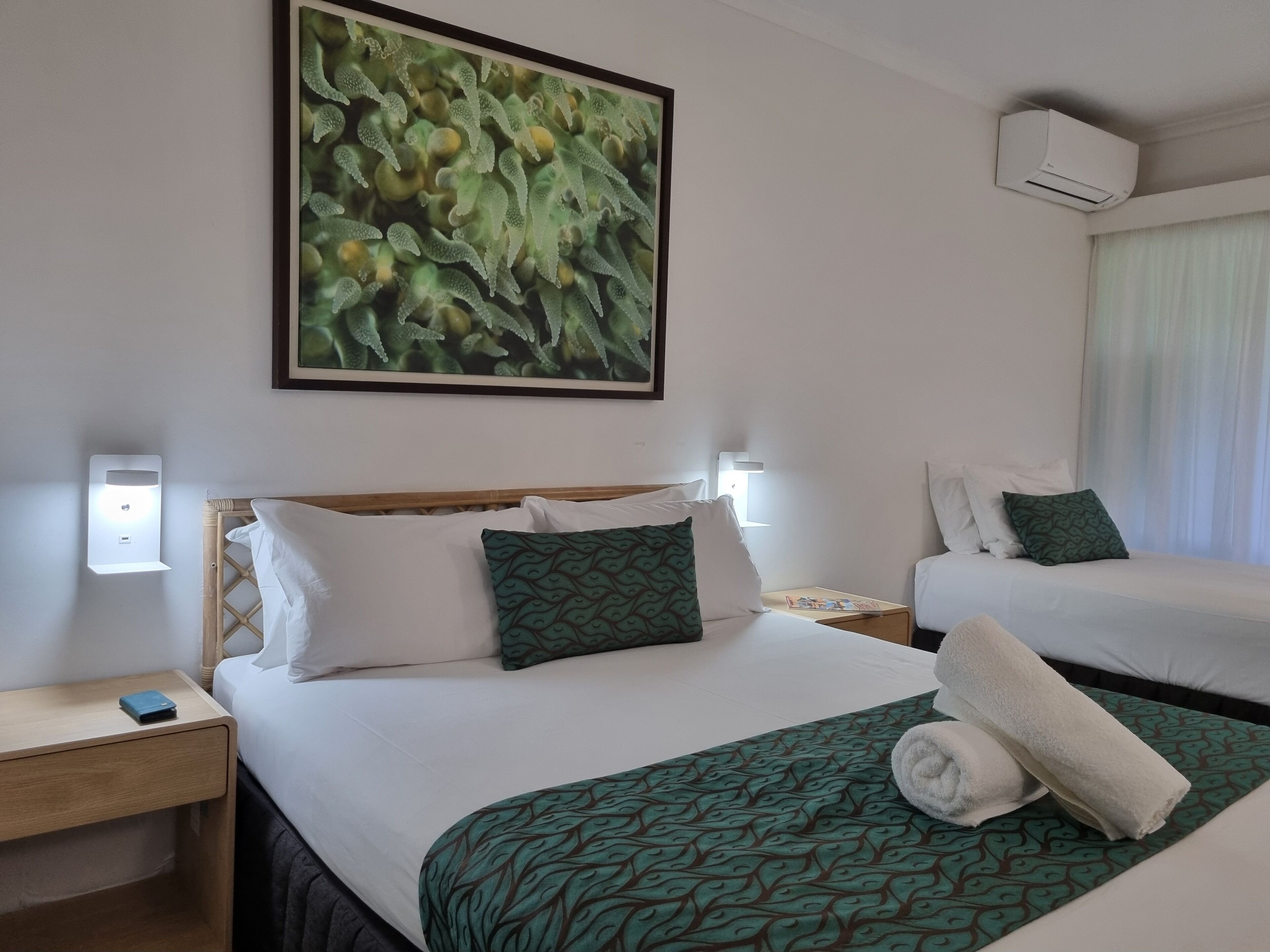 Habitación de hotel con dos camas, una mesita de noche, aire acondicionado montado en la pared y un cuadro sobre las camas.