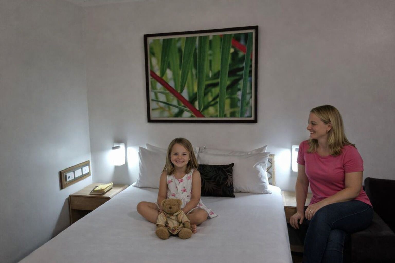 A hotel room with a bed, a nightstand, a bedside table, and a wall-mounted painting.