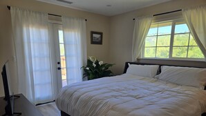 A bedroom with a bed, a TV on a stand, a window with curtains, and a door with a view of greenery. - Awesome Three-bedroom Retreat on 1.25 acres in Coarsegold with Trails and Views (Coarsegold)