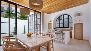A spacious dining area with a marble table, wooden chairs, and a view of the outdoors. - Villa Lila (Canggu)