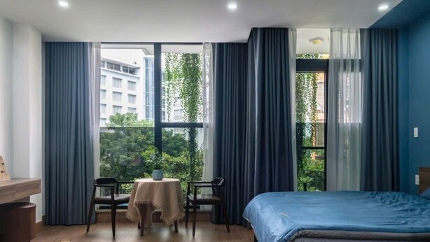 Una habitación de hotel con una cama, una mesita con una silla y un ventanal con cortinas.