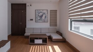 Un salon moderne avec un plancher en bois, un banc intégré, une œuvre d’art accrochée au mur et une fenêtre équipée de stores.